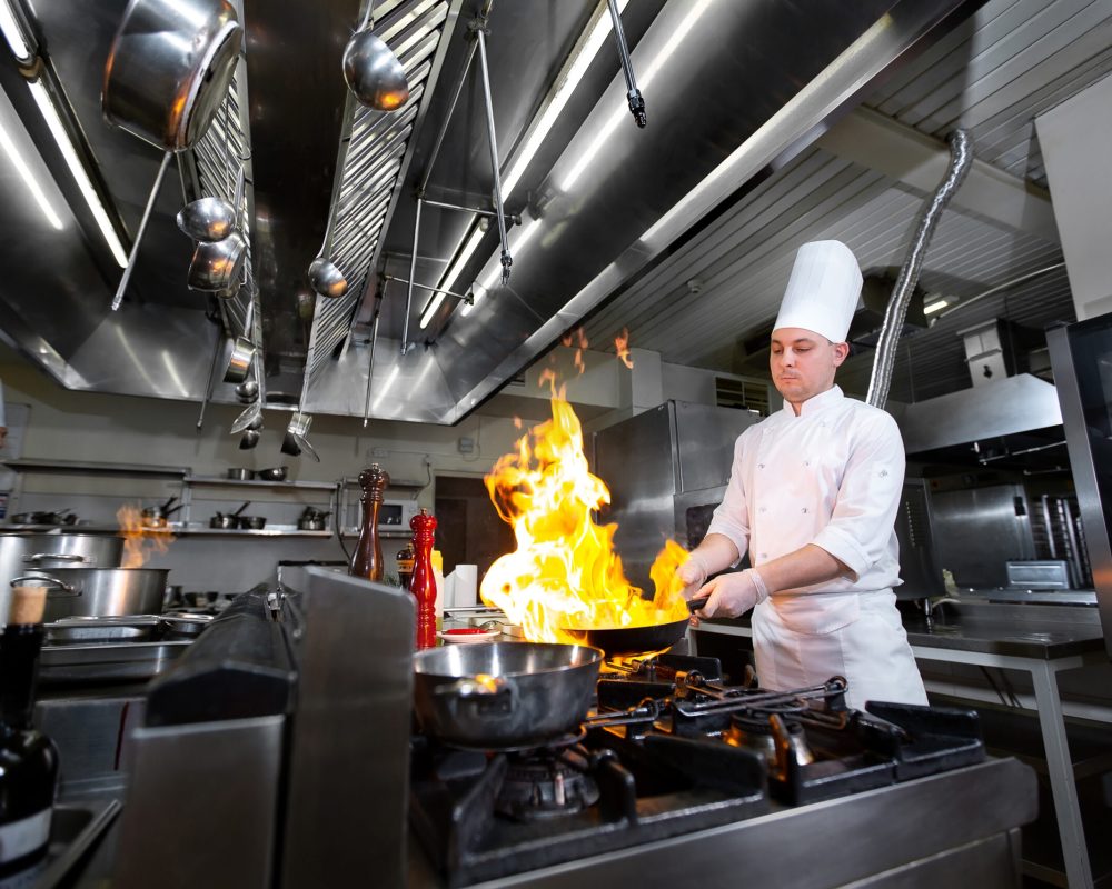 Chef cooking with flame in a frying pan on a kitchen stove