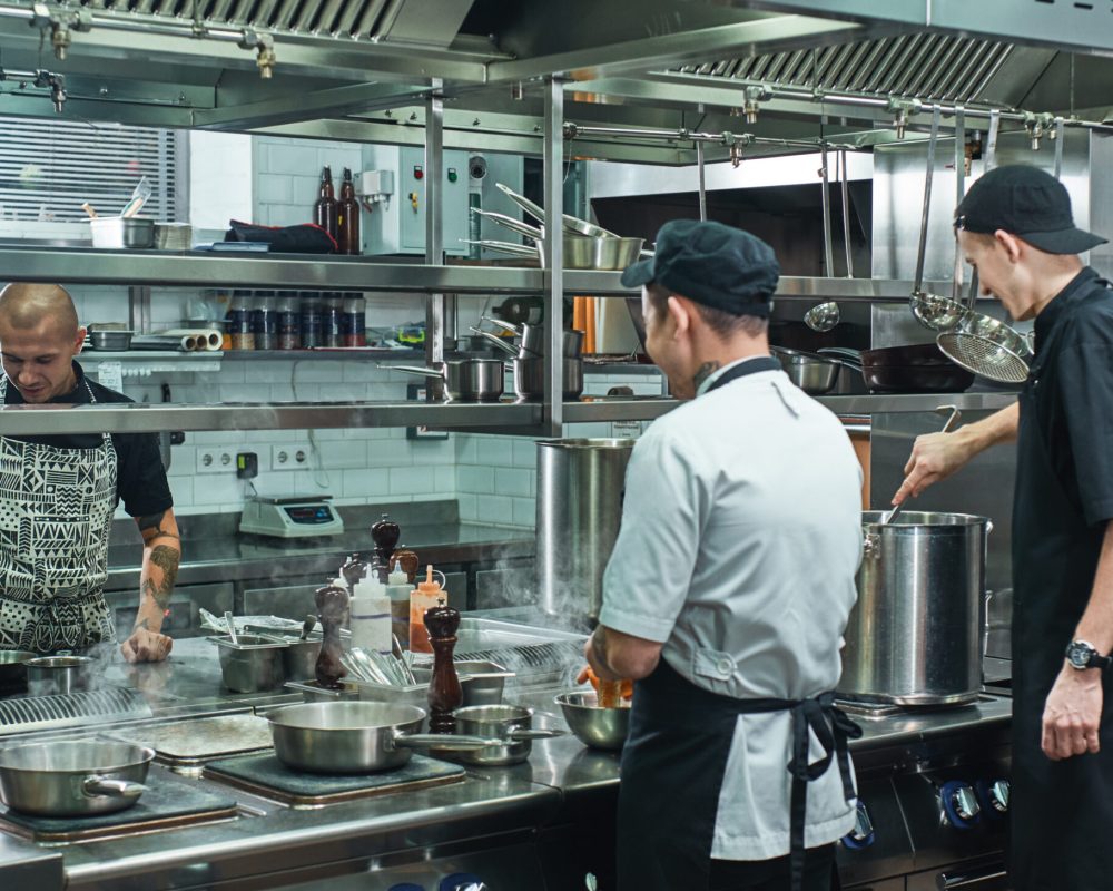 Cooking process. Professional team of chef and two young assistant preparing food in a restaurant kitchen. Teamwork